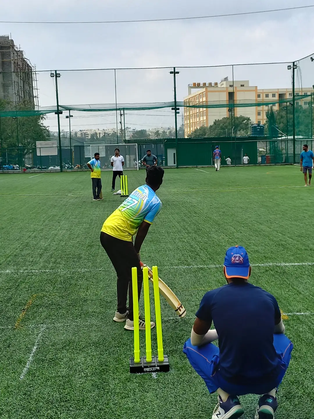 Daytime box-cricket match on the netted turf at Coliseo Noble Residency